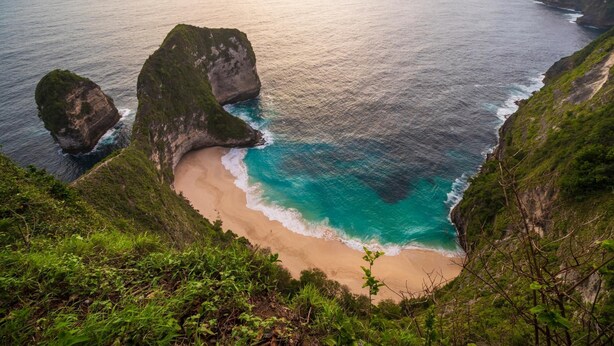 A coastal landscape with a beach, cliffs, and a clear view of the ocean.