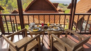 A balcony with wooden furniture and a table set for breakfast, overlooking a row of traditional buildings with red-tiled roofs.