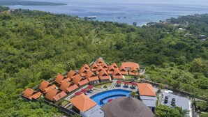 An aerial view of a resort with multiple bungalow-style buildings, a swimming pool, and a view of the ocean.