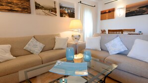 A living room with a beige sofa, a glass coffee table with decorative items, and wall-mounted artwork. - Belvedere (Arzachena)