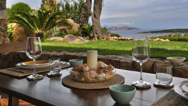 A table set for a meal with a view of the sea, a candle centerpiece, and a bowl of seashells. - Belvedere (Arzachena)