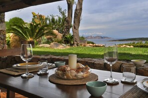 A table set for a meal with a view of the sea, a candle centerpiece, and a bowl of seashells. - Belvedere (Arzachena)