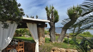 A patio with a table and chairs, a stone wall, and a view of the sea. - Belvedere (Arzachena)