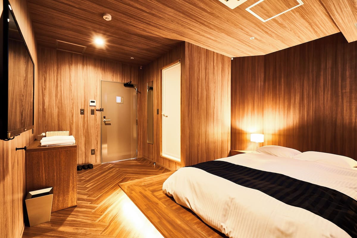 Et hotelværelse med træpaneler, en seng med sengetøj i hvid og sort, et natbord med en lampe og en dør med en frakke hængende på den.