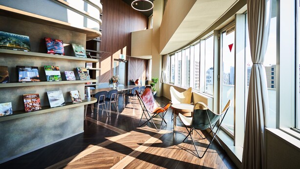 Un intérieur moderne avec un plancher en bois, un comptoir d’accueil avec des brochures et un espace détente comprenant des chaises et une table.