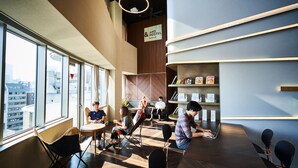 Un café moderne avec de grandes fenêtres, un intérieur en bois et une enseigne indiquant « And Hostel ».