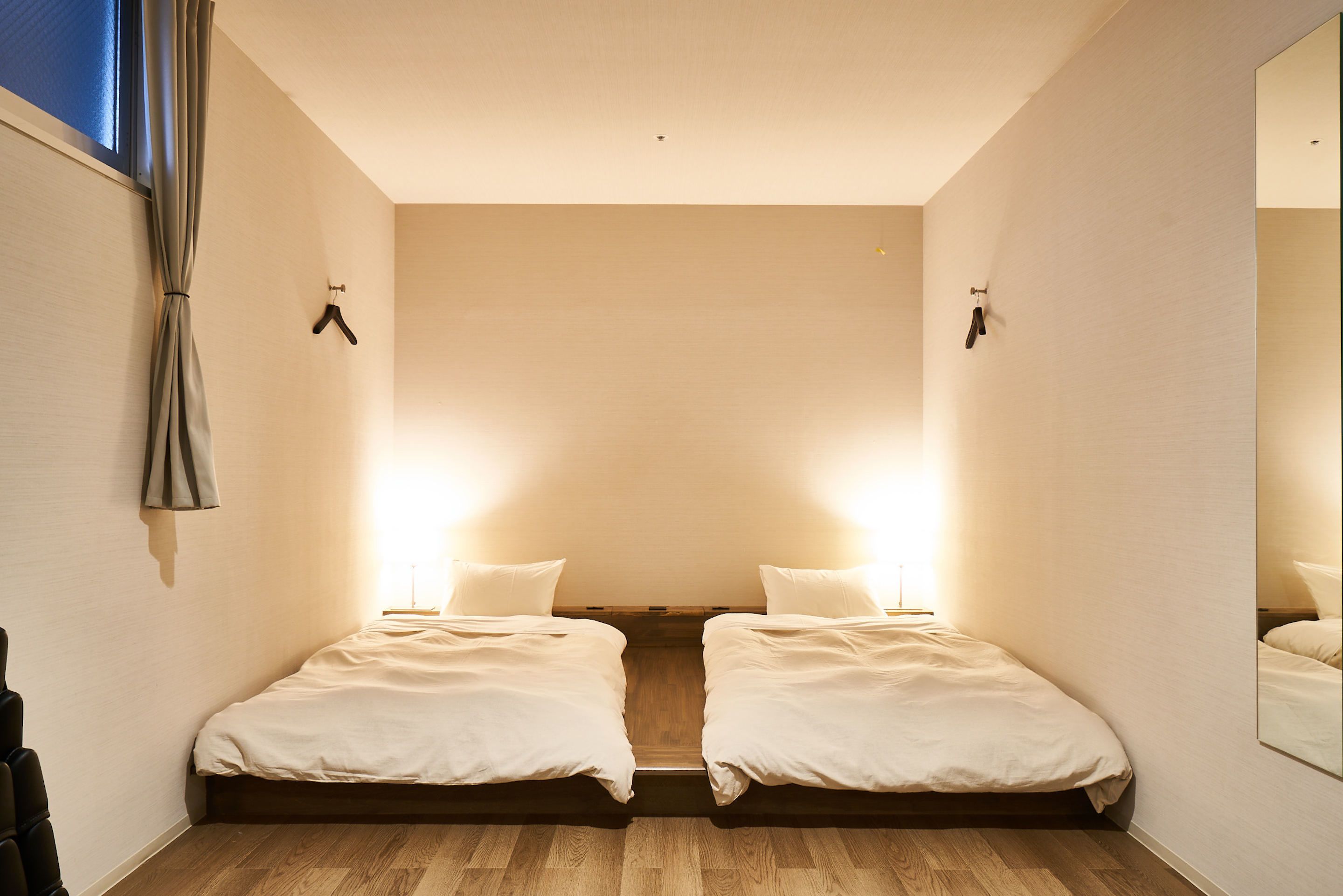 A bedroom with two beds, a wooden floor, and a large mirror on one wall.
