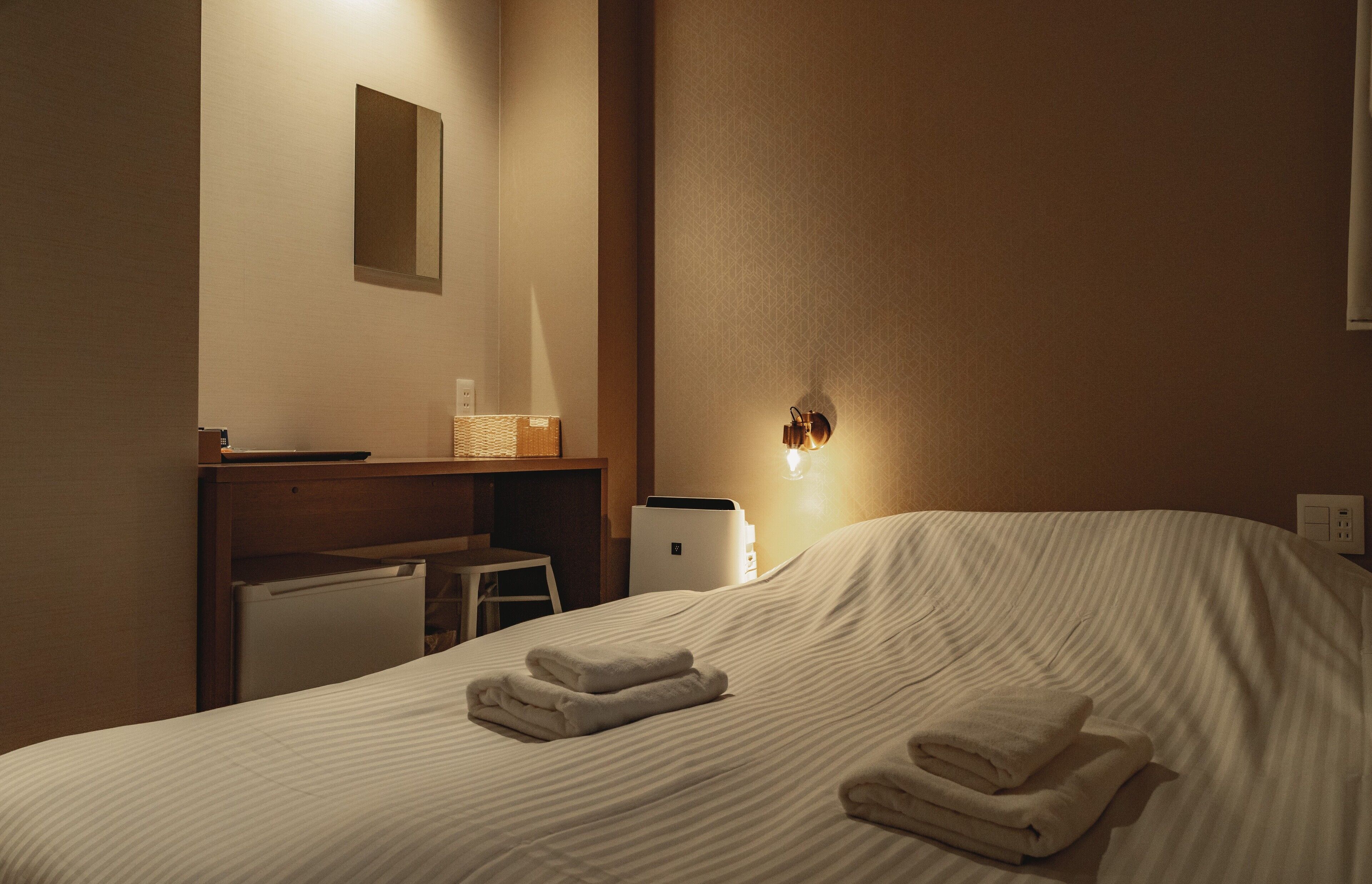 Una camera d'albergo con un letto, una scrivania, una sedia e una lampada a parete.