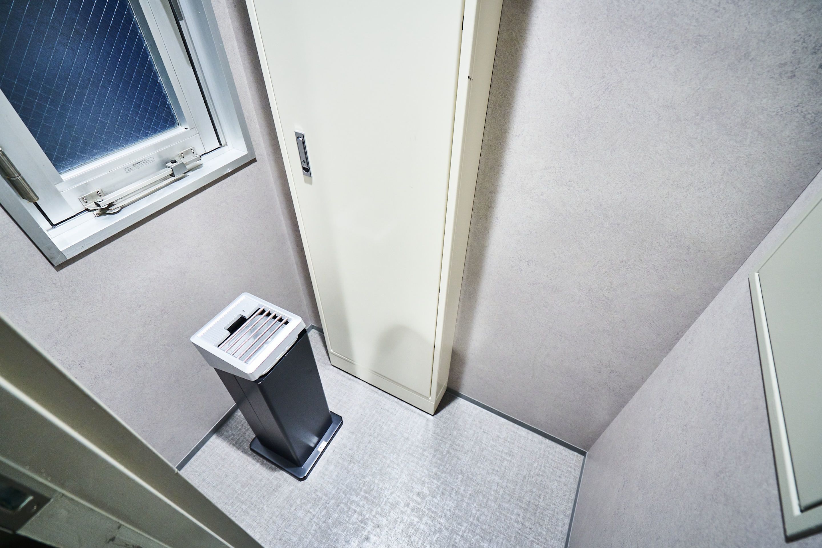 A narrow hallway with a white door, a window with a grid pattern, and a trash bin.