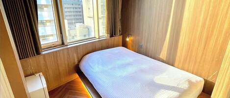 A bedroom with a bed, a window, and a wooden floor.
