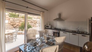 Une cuisine moderne avec un mur en pierre, un coin repas avec une table et des chaises, et une vue sur l’extérieur.
