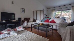Un salon comprenant un canapé, une table basse, un téléviseur et donnant sur l’extérieur.