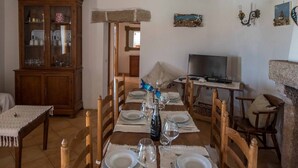A dining area with a wooden table set for four, a television, and a stone fireplace. - Villa Noelia (Arzachena)