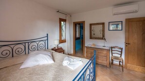 A bedroom with a bed, a dresser, a chair, a mirror, and a door. - Villa Noelia (Arzachena)
