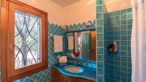 A bathroom with a wooden door, a window, a sink, and a mirror. - Villa Noelia (Arzachena)