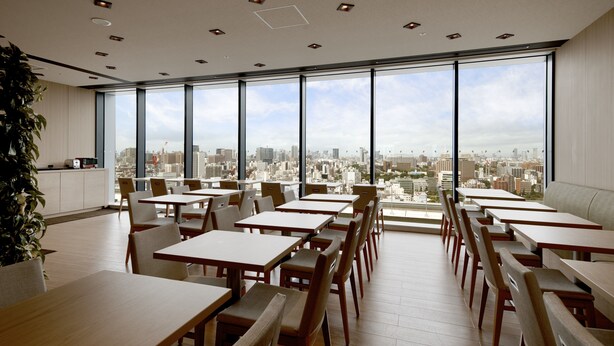 A modern dining area with large windows offering a city view. Tables and chairs are arranged neatly. - Hotel Crown Hills Ueno Premier (Tokyo)