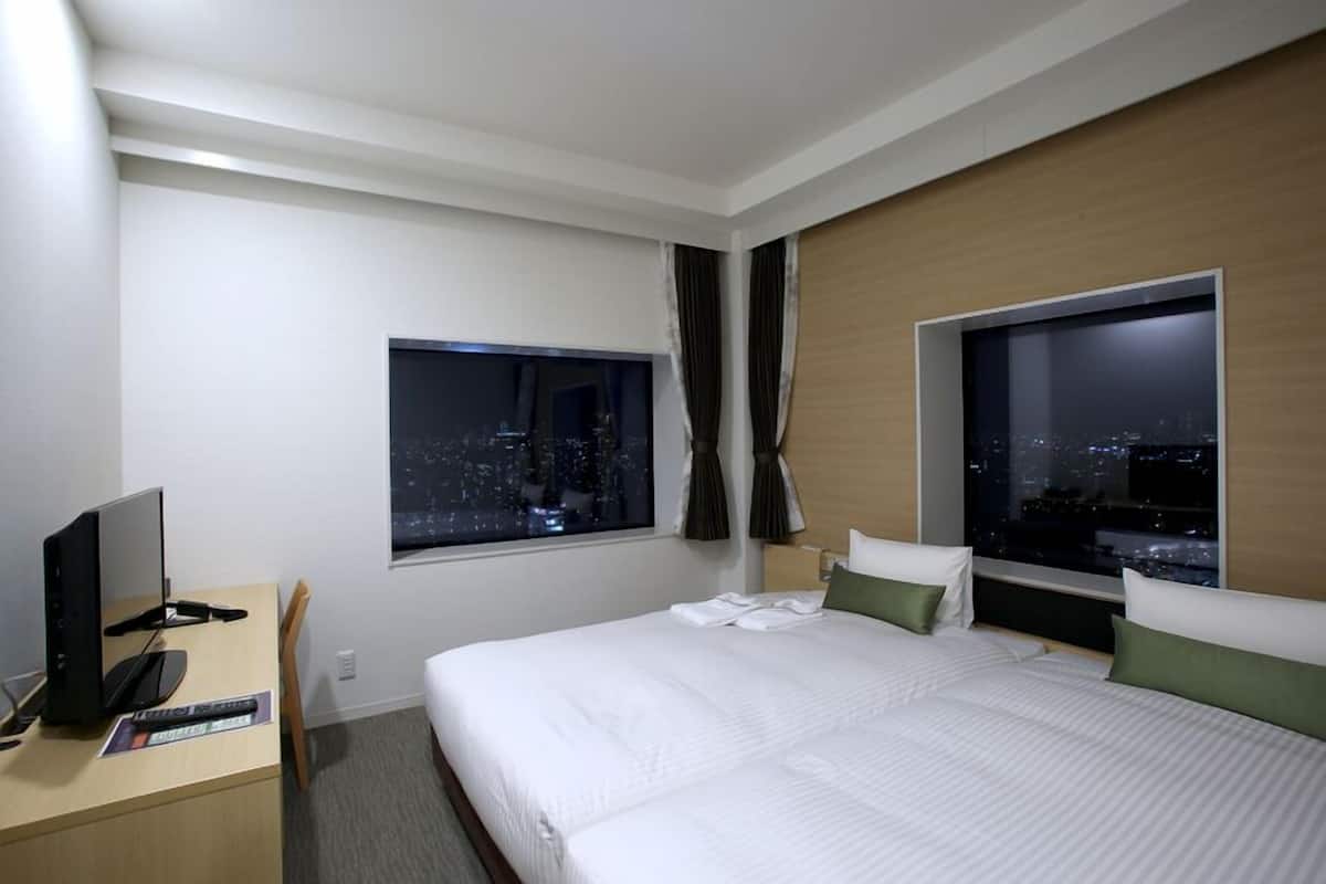 Een hotelkamer met een bed, een bureau met een computer, en uitzicht op een stadsbeeld bij nacht.