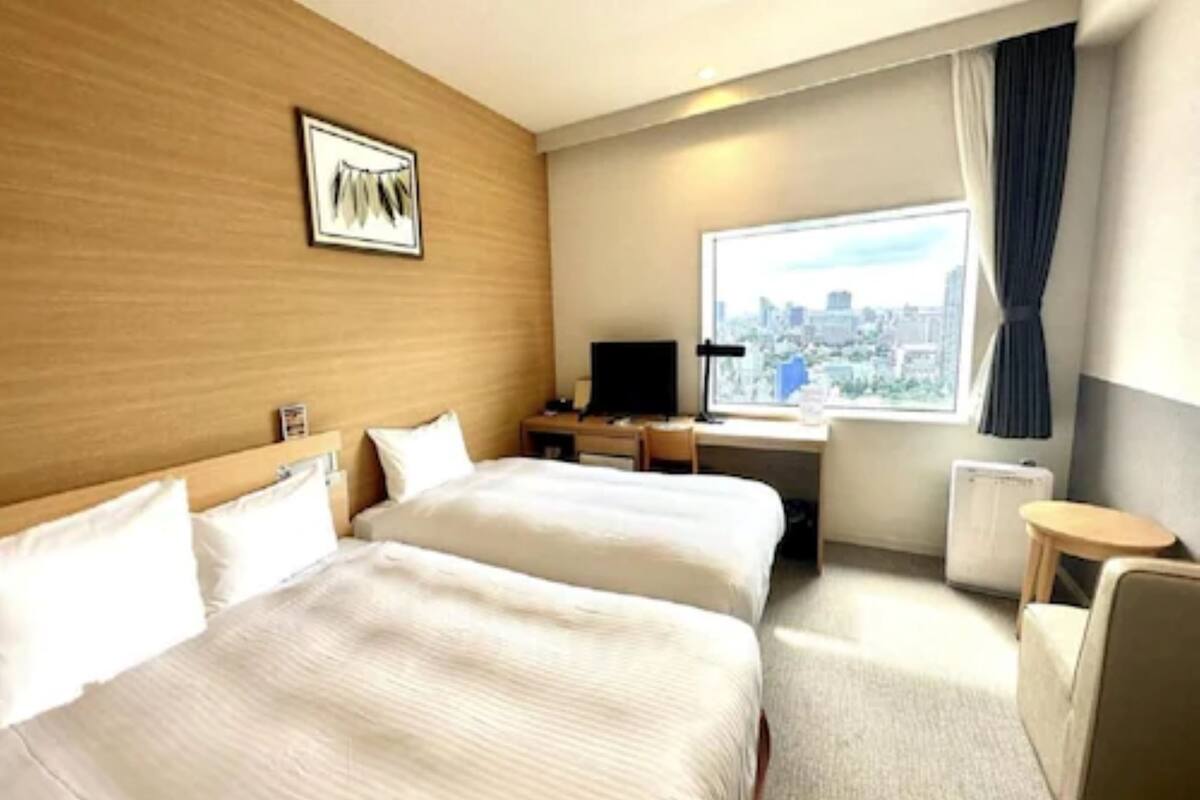 Hotelkamer met twee bedden, een bureau, een stoel, een televisie en een raam met uitzicht op de stad.