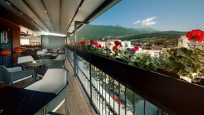 Un balcón con mobiliario exterior, vistas a la ciudad y una montaña al fondo.