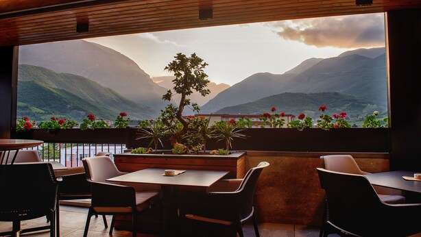 Un restaurante con un amplio ventanal que ofrece vistas a un paisaje montañoso. Hay varias mesas y sillas dispuestas para comer.