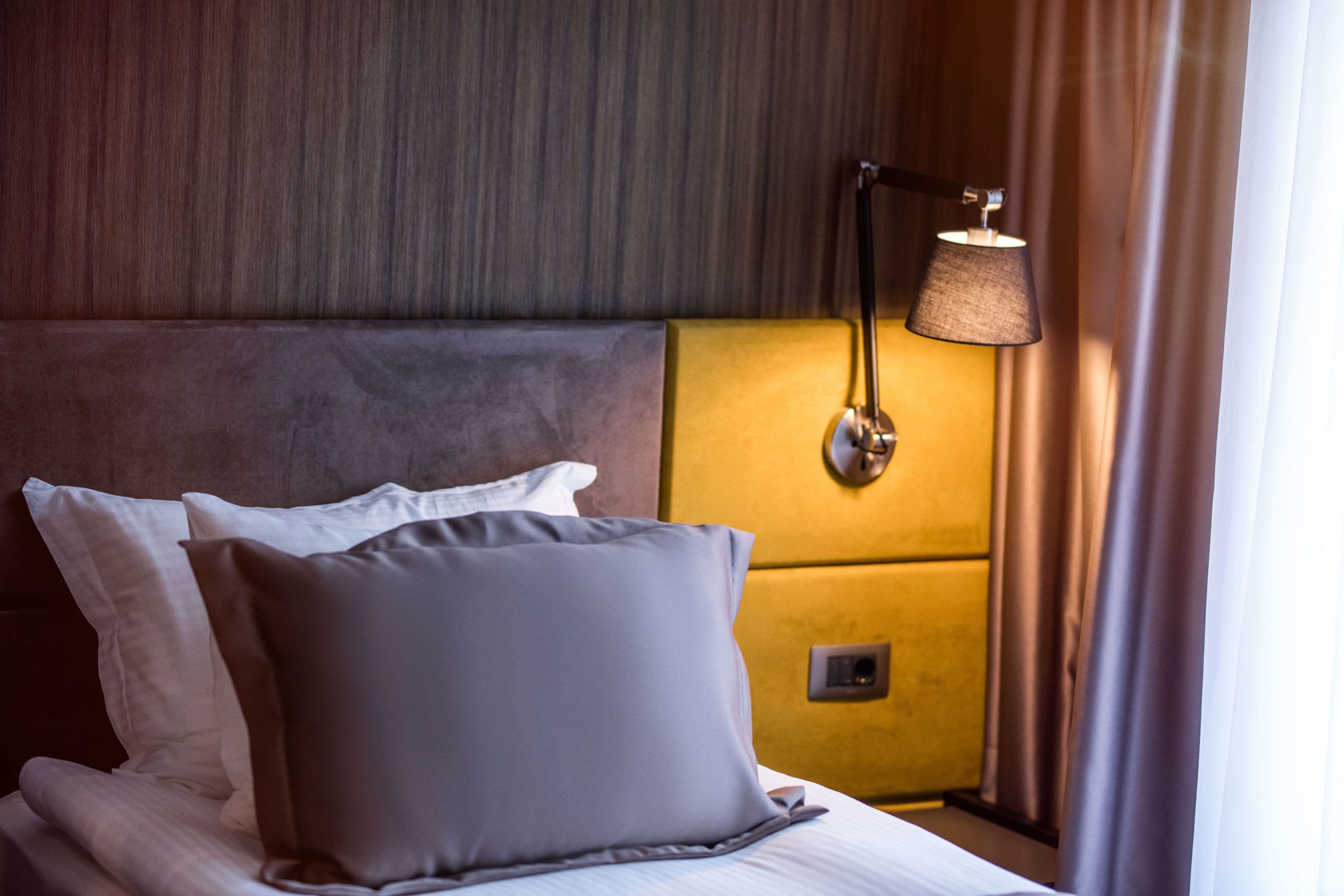 A hotel room with a bed, pillows, a headboard, a bedside lamp, and a nightstand.