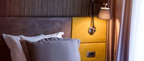 A hotel room with a bed, pillows, a headboard, a bedside lamp, and a nightstand.