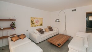 A modern living room with a white sofa, a wooden coffee table, and a painting on the wall. - Oleandri 101 (Arzachena)