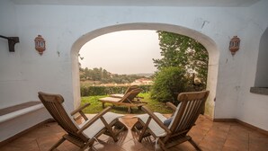 A terrace with two wooden lounge chairs and a table, an archway leading to a garden with a view of the countryside. - Oleandri 101 (Arzachena)