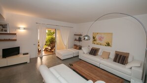 A modern living room with a sofa, a coffee table, and a TV. There is a sliding door leading to an outdoor area. - Oleandri 101 (Arzachena)