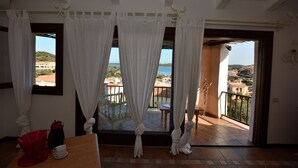 A balcony with white curtains, a red umbrella, and a table with a white cup and saucer. - Oleandri 238 (Arzachena)
