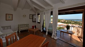 A room with a wooden table and chairs, a bench, and a balcony with a view of the sea. - Oleandri 238 (Arzachena)