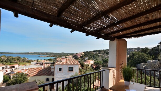 A balcony with a view of a coastal town, a table, and a potted plant. - Oleandri 238 (Arzachena)