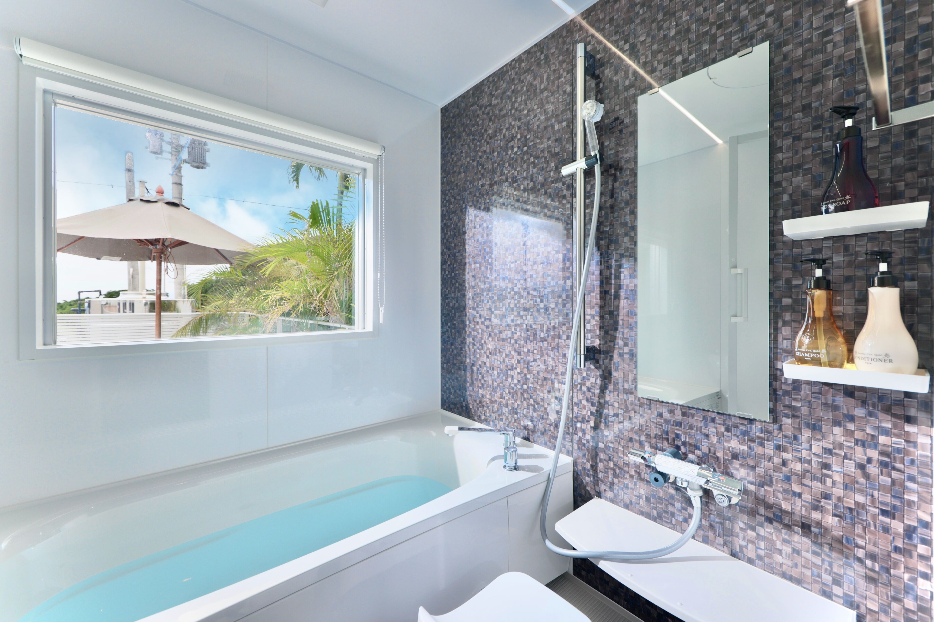 A modern bathroom with a large bathtub, a shower, and a window with an umbrella.