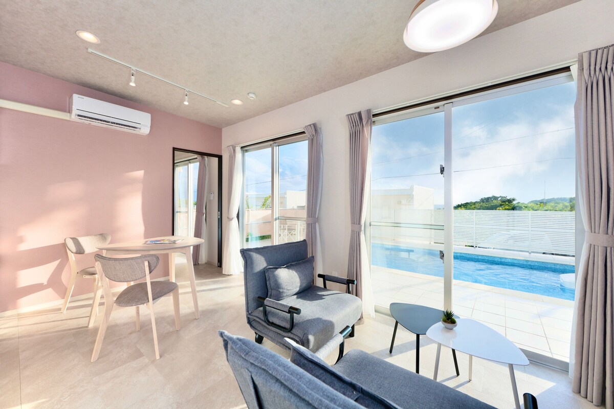 Una habitación de hotel moderna con balcón, vistas a la piscina y zona de estar con mesa y sillas.