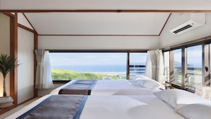 Ein Hotelzimmer mit zwei Betten, großen Fenstern, einem Blumentopf und einer Klimaanlage.