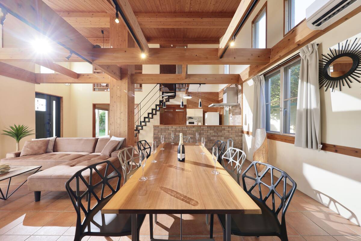 Un vaste espace dédié à la salle à manger, avec une longue table en bois, de nombreuses chaises et une bouteille de vin placée au centre.