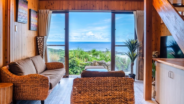 Ein Holzinterieur mit einer Couch, zwei Sesseln, einem Fernseher und Blick auf den Ozean.