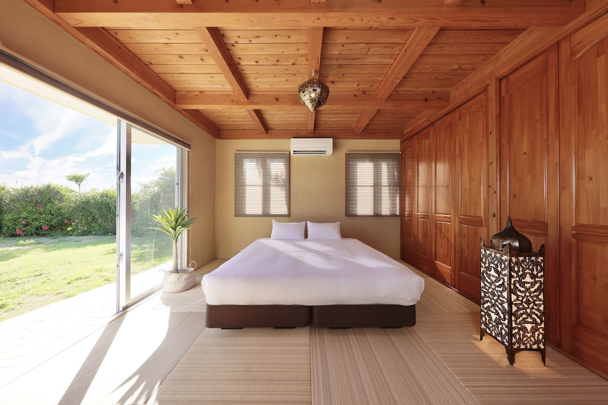 Un espacioso dormitorio con una cama grande, puertas de cristal correderas que dan a un jardín y un ventilador de techo.