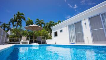 A swimming pool with a clear blue sky, palm trees, and a white building with large windows.