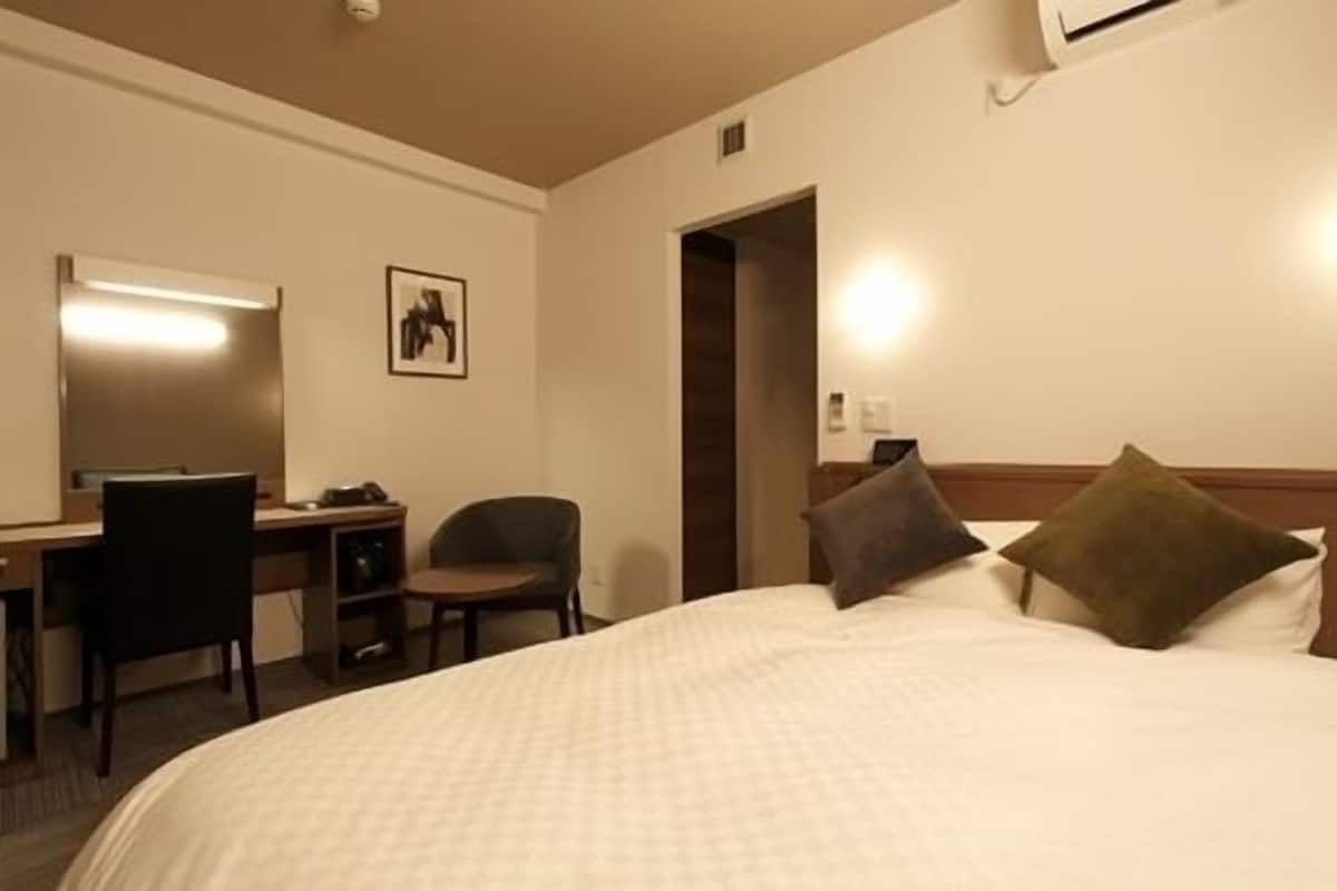 Habitación de hotel con cama, escritorio con silla, un cuadro en la pared y un equipo de aire acondicionado.