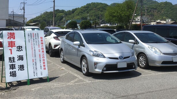 Un estacionamiento con varios coches aparcados y un cartel con texto en japonés.