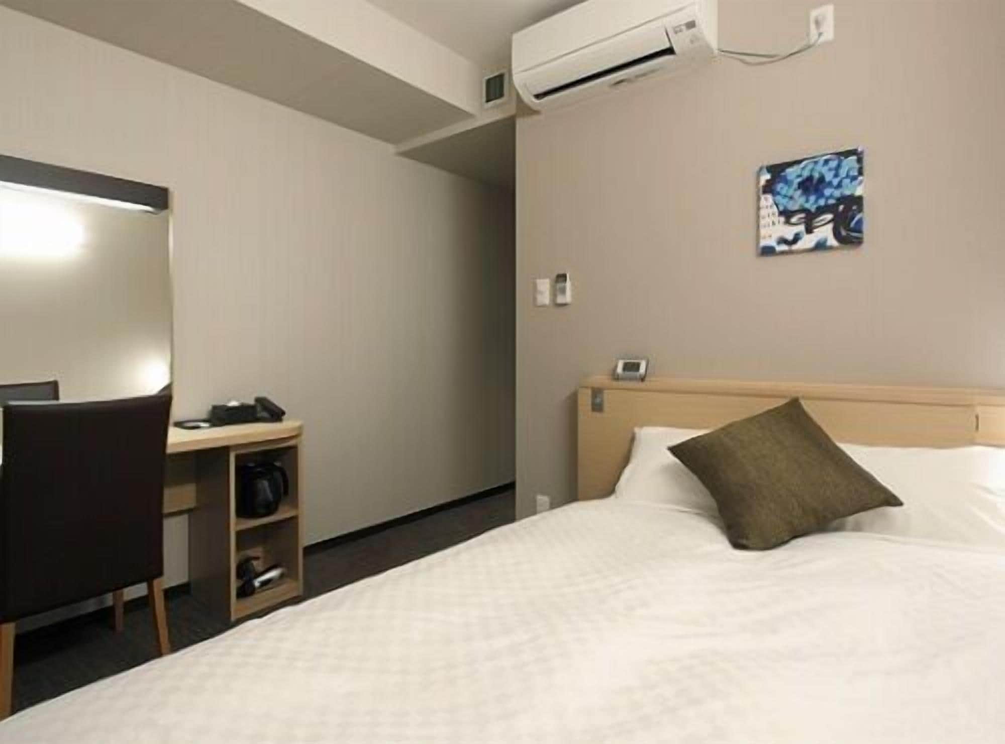 Een hotelkamer met een bed, een bureau, een stoel, een airconditioning en een telefoon aan de muur.