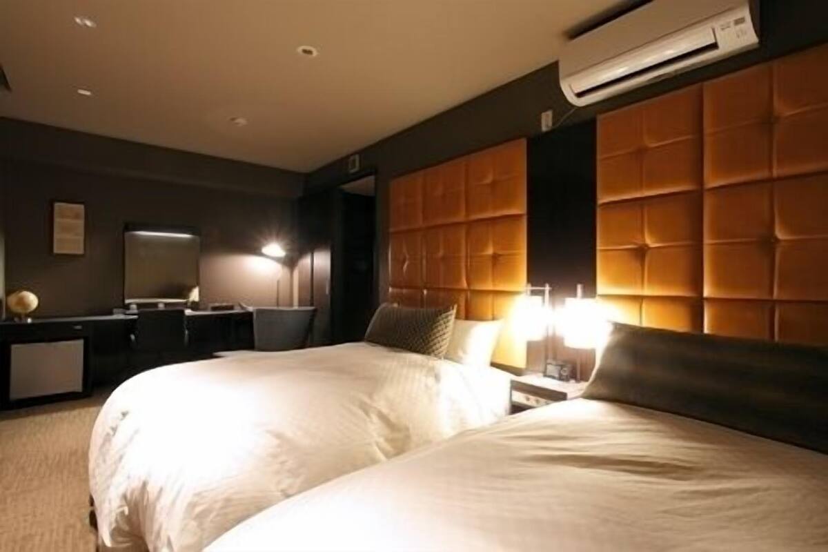 A hotel room with two beds, a desk, a chair, a mirror, and an air conditioning unit.