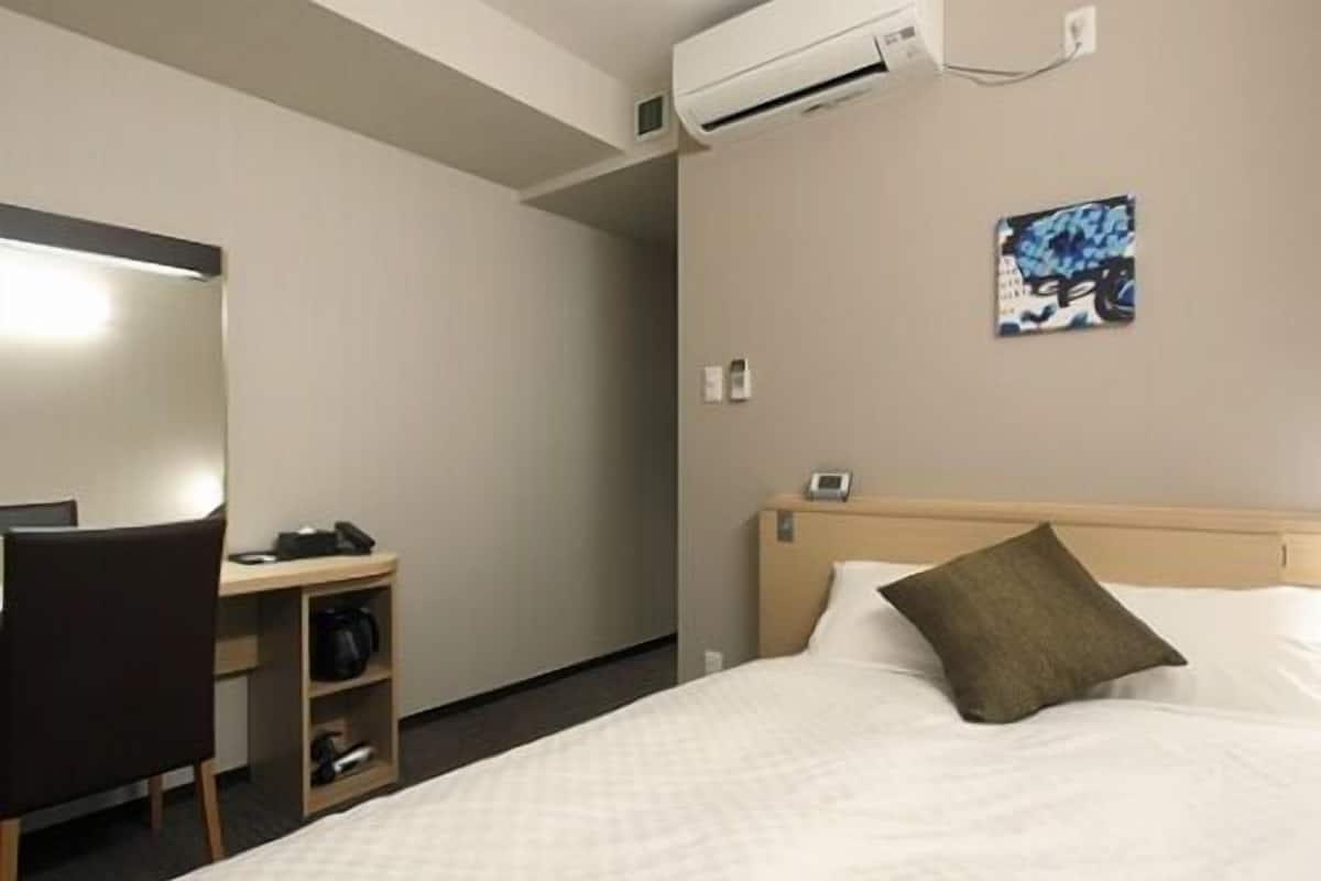 Habitación de hotel con cama, escritorio, silla, aire acondicionado y teléfono en la pared.