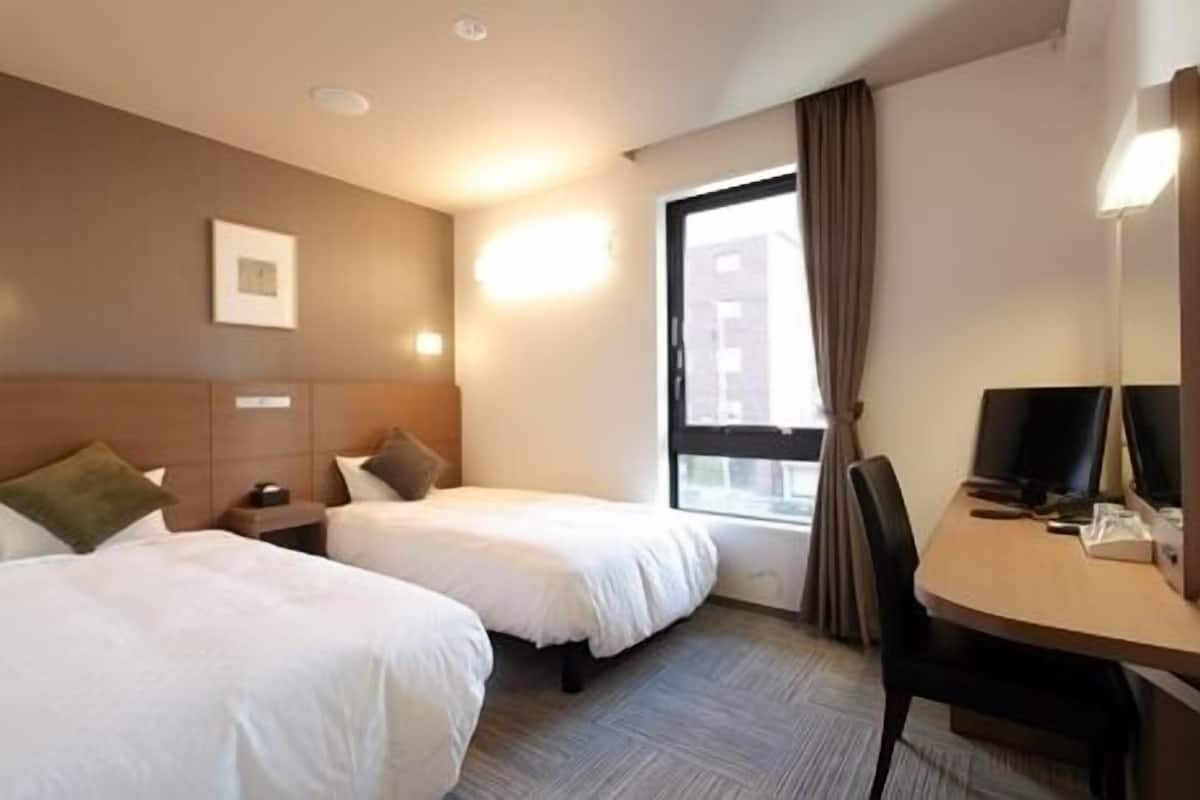A hotel room with two beds, a desk, a chair, a window with curtains, and a picture on the wall.