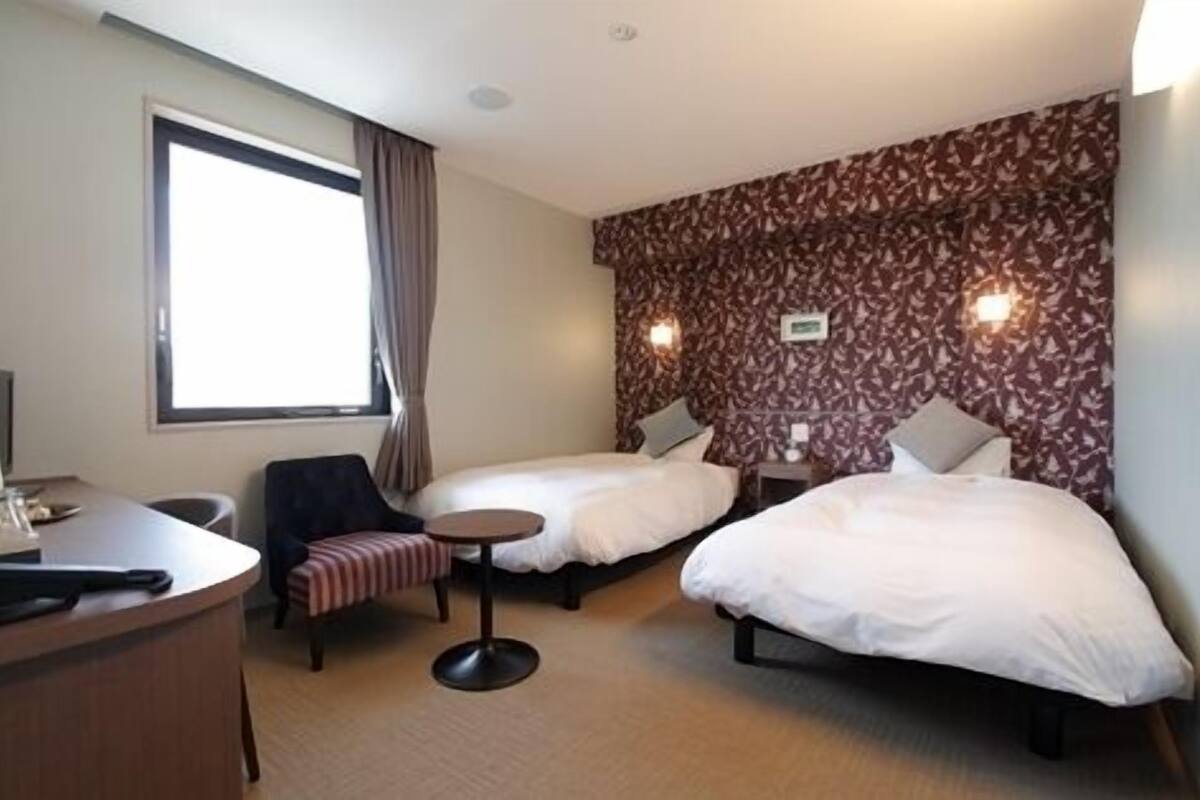 A hotel room with two beds, a desk, a chair, and a small round table.