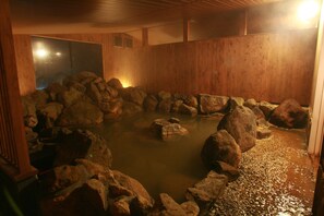 Un interior de madera con una zona de aguas termales rodeada de rocas.