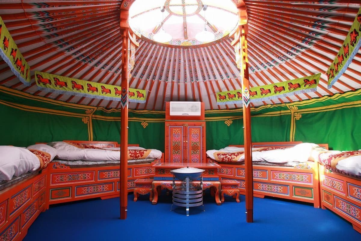 A traditional yurt with four beds, a central table, and a green curtain backdrop.