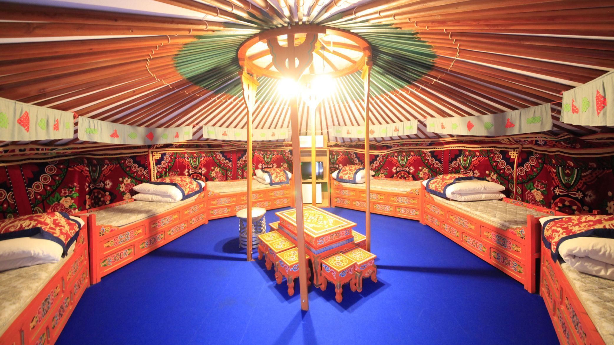 A traditional yurt with four beds, a central wooden structure, and a blue floor.