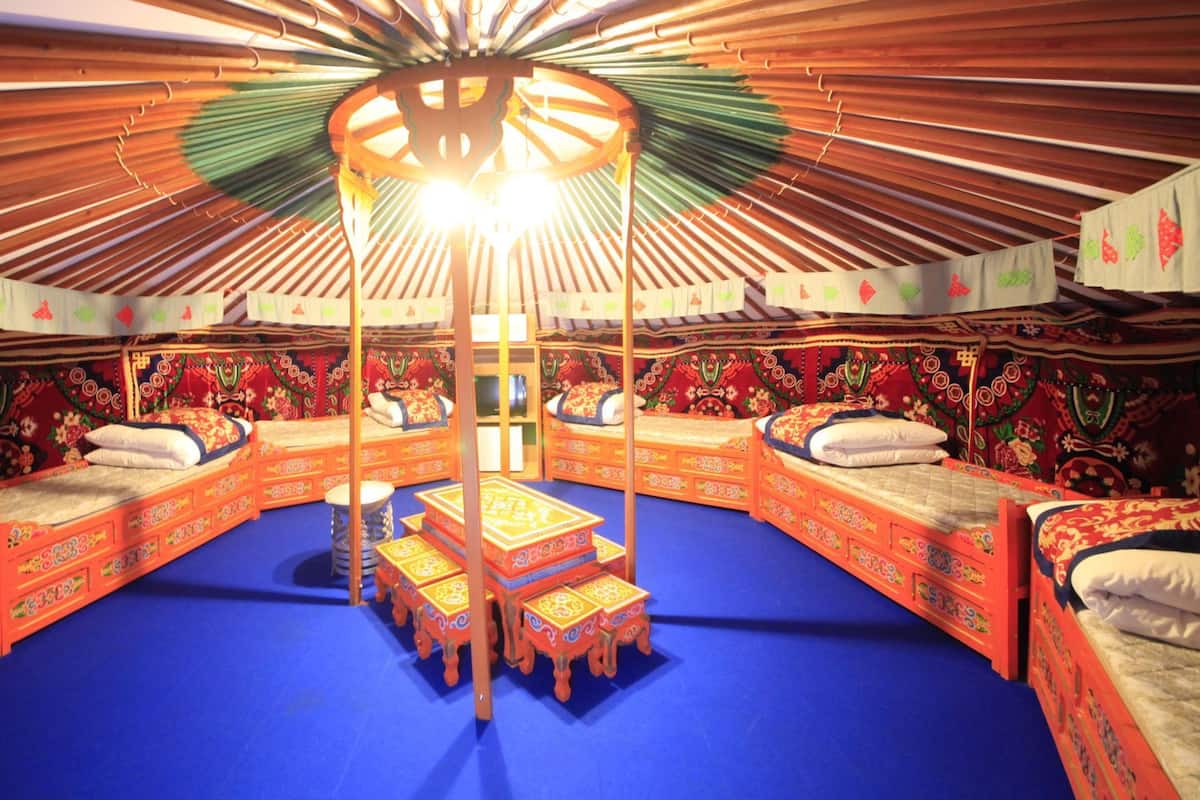 A traditional yurt with four beds, a central wooden structure, and a blue floor.